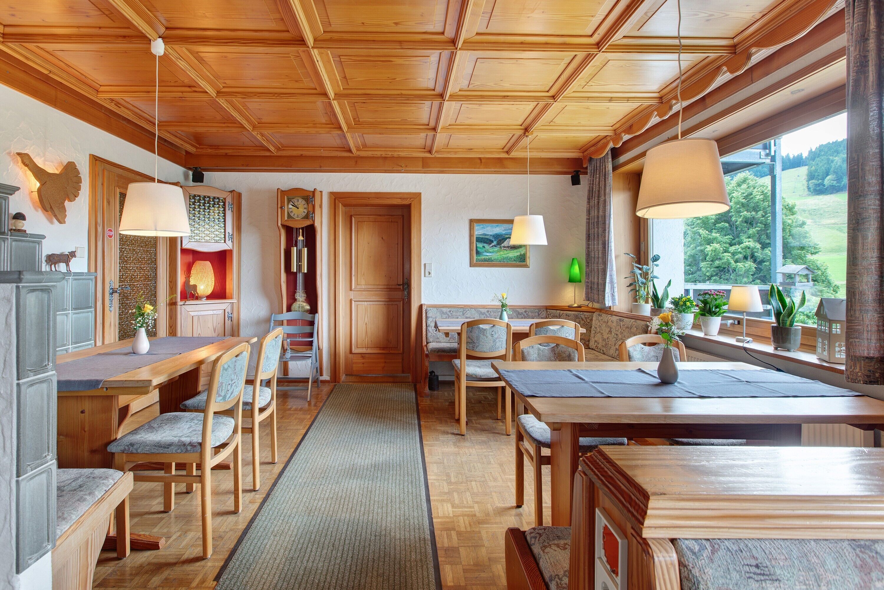 Un interno in legno con zona pranzo, sedie, tavolo, tappeto, panchina, divano, una finestra con vista e un orologio appeso al muro.