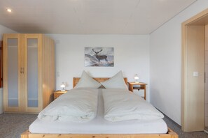 Un dormitorio con cama, dos mesitas de noche con lámparas, un armario de madera y un cuadro de un ciervo colgado en la pared.