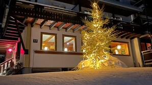 Paisagem coberta de neve com um pinheiro de Natal iluminado em frente a um edifício.
