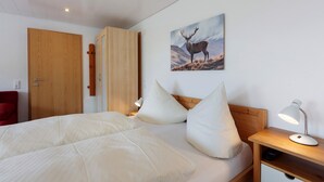 Quarto com cama, almofadas, mesa de cabeceira com abajur, porta de madeira e quadro de um veado fixado na parede.