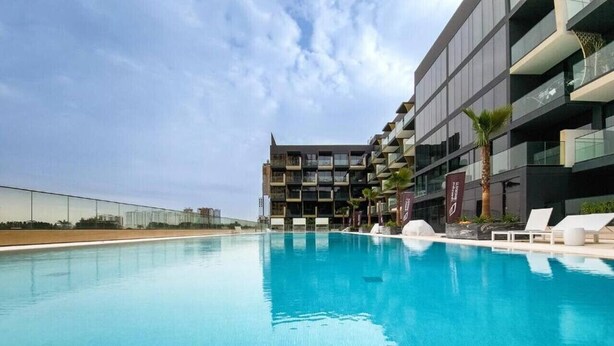 A modern hotel with a large swimming pool, multiple balconies, and lounge chairs. - Binghatti Crescent - Two Bed with Pool View in JVC (Jumeirah Village Circle)