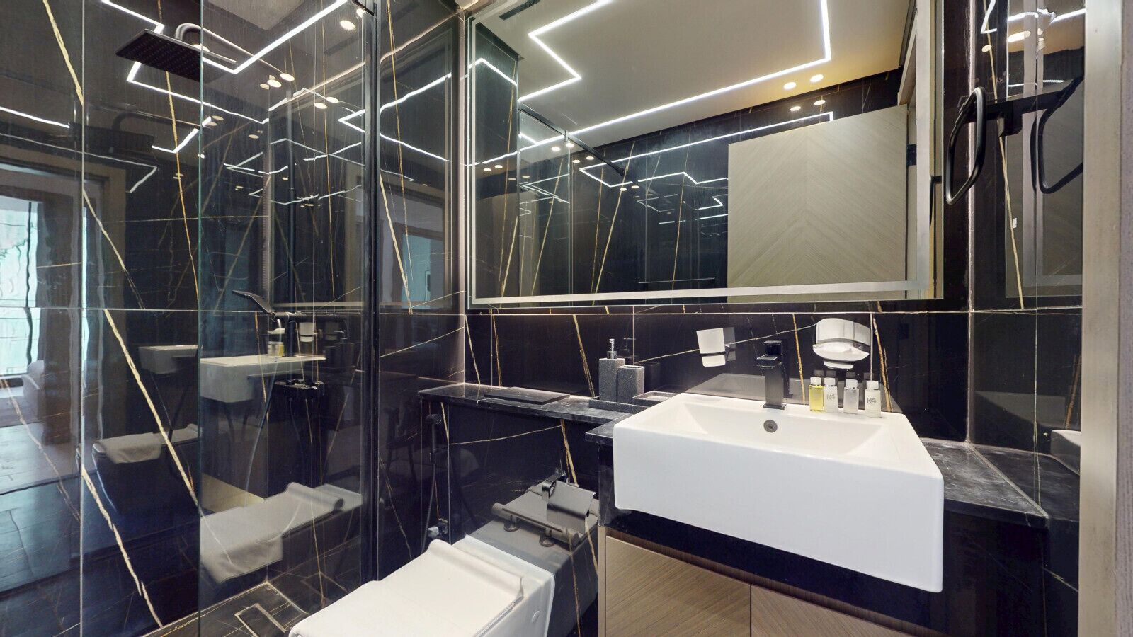 Een moderne badkamer met een wit wastafelmeubel, wanden van zwart marmer en een douchecabine van glas.