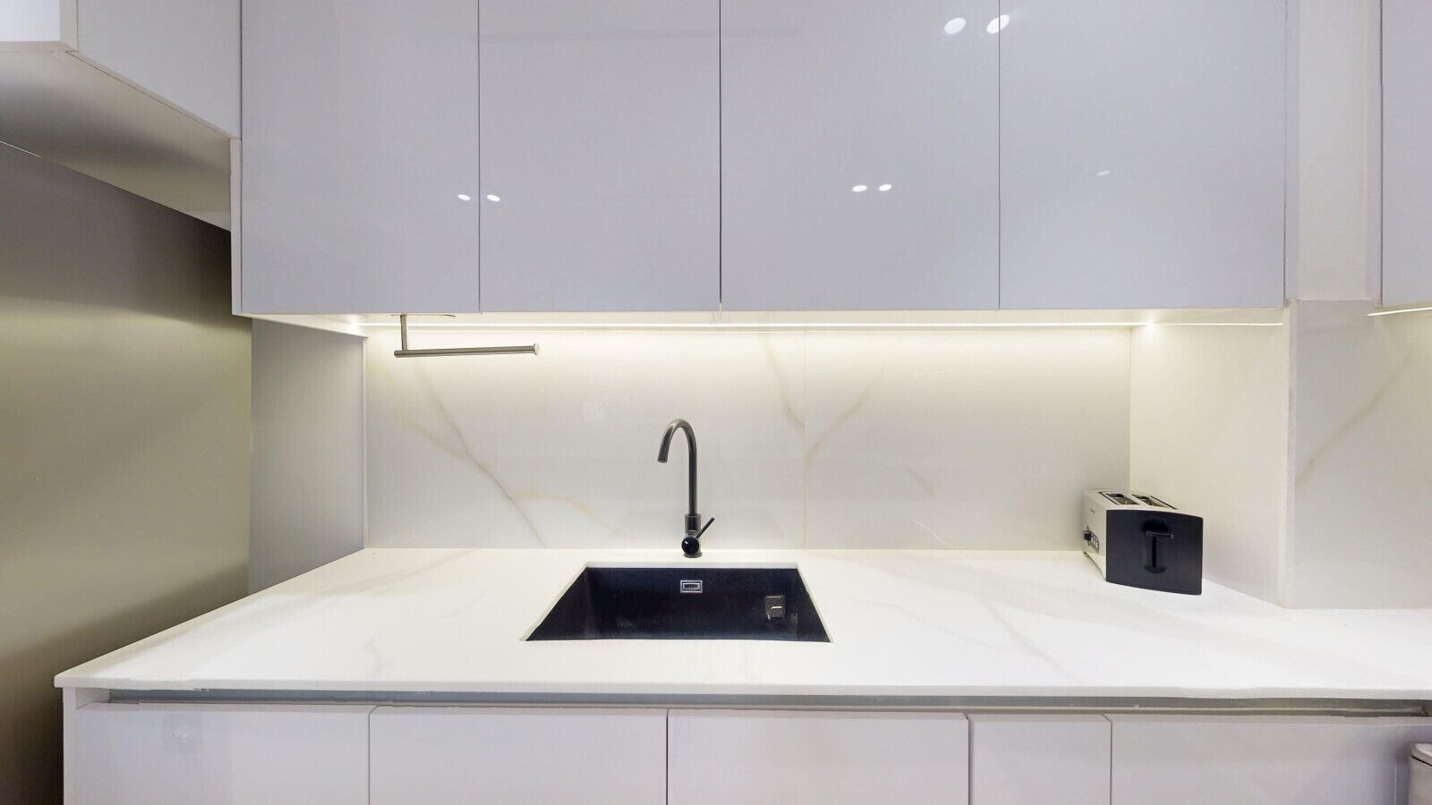 A modern kitchen with a sleek black sink, white marble countertop, and minimalist cabinetry.