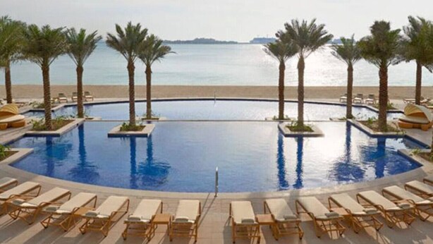 Ein Pool mit Palmen und Liegestühlen mit Blick auf einen Strand.
