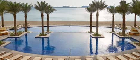 Ein Pool mit Palmen und Liegestühlen mit Blick auf einen Strand.