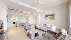Ein modernes Wohnzimmer mit einer Couch, Sesseln und einem Couchtisch. Im Hintergrund ist eine Küchenzeile mit Barhocker zu sehen.