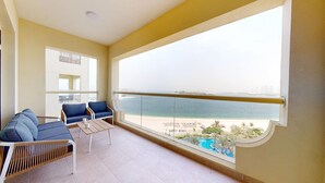Ein Balkon mit Blick auf Strand und Pool, ausgestattet mit einer Couch, Sesseln und einem Tisch.