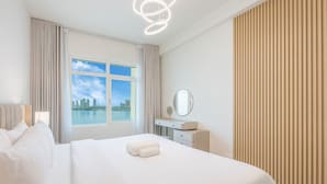 Ein Hotelzimmer mit einem großen Bett, einem Nachttisch mit Spiegel, einem Fenster mit Blick auf die Stadtlandschaft und einer Deckenleuchte.