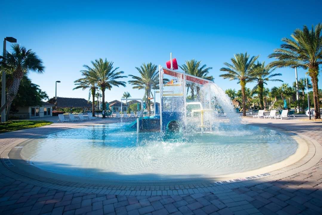 A circular water feature with a central fountain, surrounded by palm trees and lounge chairs.