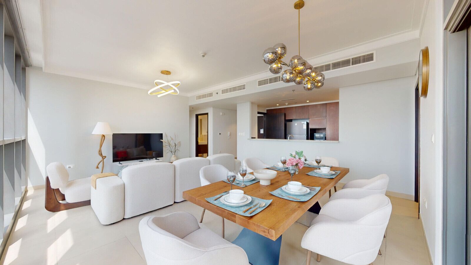 A modern dining area with a wooden table set for six, surrounded by white chairs.