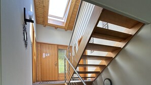 Eine Holztreppe mit Metallgeländer, das zu einer Zwischenebene im zweiten Stock führt.