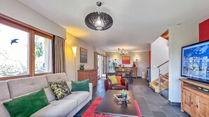 Ein modernes Wohnzimmer mit Sofa, Couchtisch und Fernseher. Im Hintergrund befindet sich eine Essecke mit einer Küche.