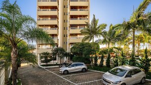 A parking area with two cars, a tall building with balconies, and palm trees.