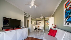 A modern living room with a white sofa, a red pillow, a flat-screen TV, and a ceiling fan.