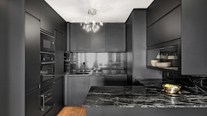 A modern kitchen with dark cabinetry, a marble countertop, and a built-in oven. - Stylish 2BR Near Faubourg Saint-Honoré (Paris)