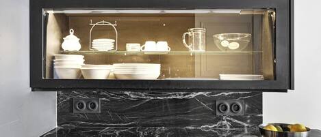 A kitchen with a black marble countertop, a glass display cabinet containing white dishes, and a bowl of lemons on the counter.