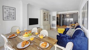 A dining area with a wooden table set for breakfast, a sofa with blue cushions, and a kitchen in the background. - Stylish 2BR Near Faubourg Saint-Honoré (Paris)