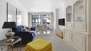 A modern living room with a sofa, ottoman, TV, and a dining area with chairs and a table. - Stylish 2BR Near Faubourg Saint-Honoré (Paris)