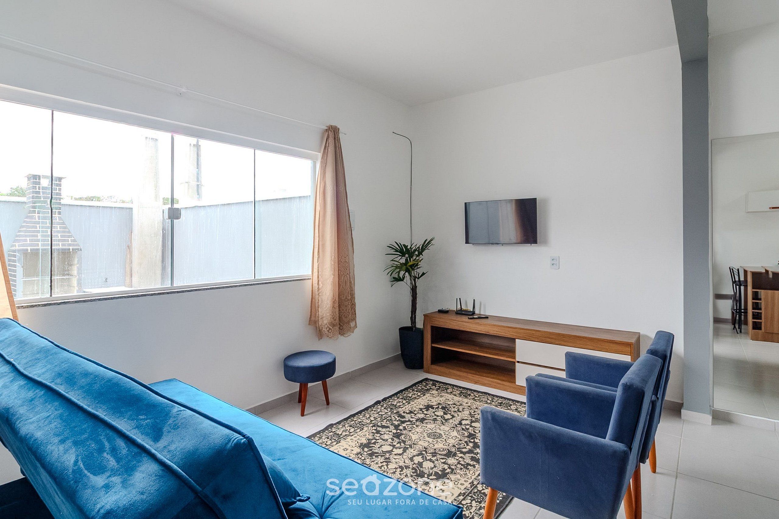 Una sala de estar moderna con un sofá azul, un mueble bajo para televisión de madera y un ventanal grande.