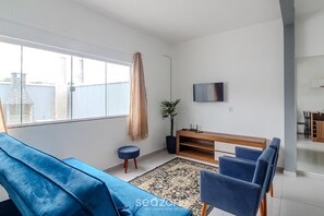 Un salon moderne avec un canapé bleu, un meuble TV en bois et une grande fenêtre.