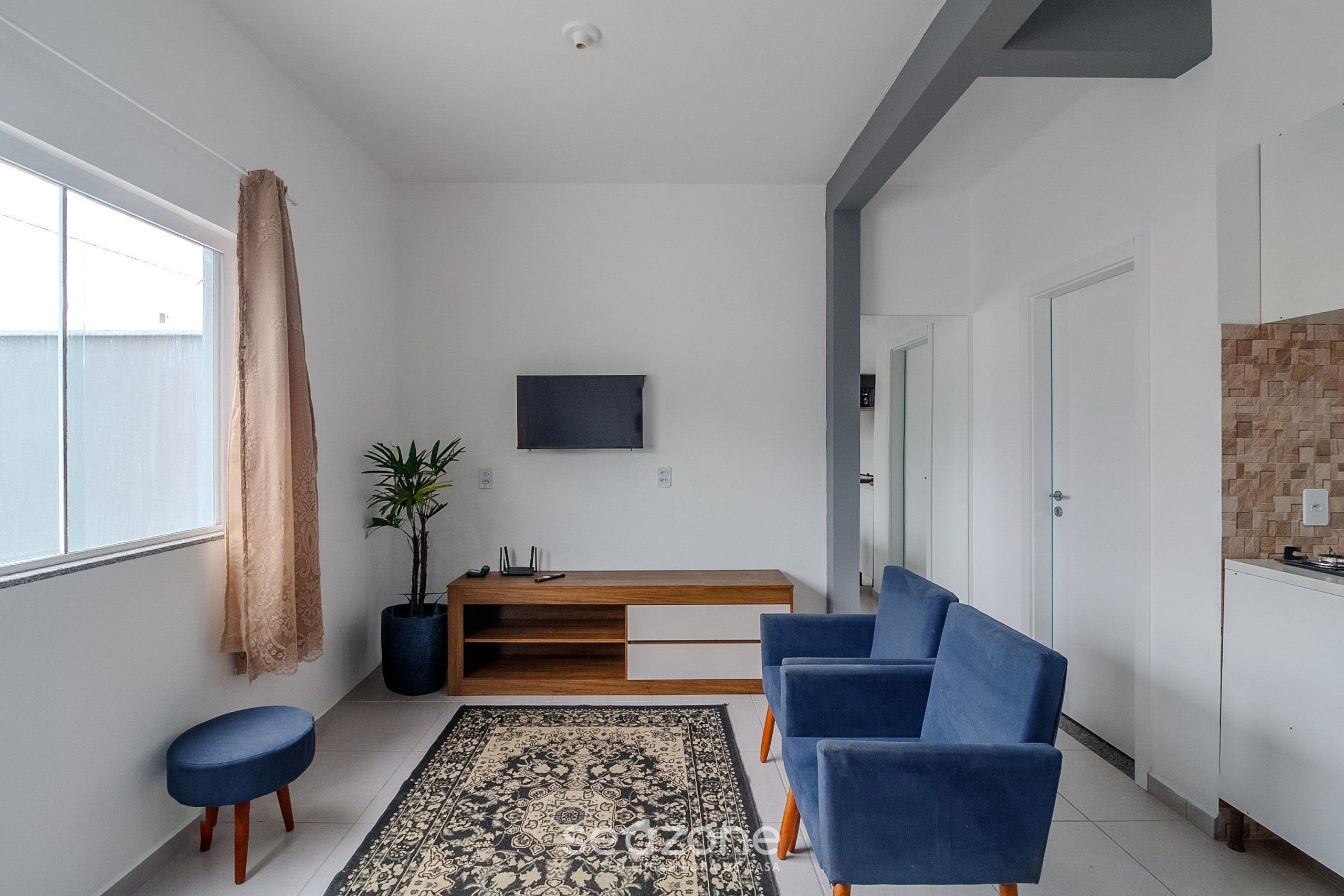 Una sala de estar moderna con un sofá, una mesa de centro, un televisor montado en la pared y una planta en maceta.