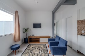Un salon moderne comprenant un canapé, une table basse, un tapis, un téléviseur fixé au mur et une plante en pot.