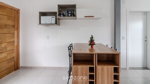 Ein modernes Zimmer mit einem Holztisch, einem kleinen Weihnachtsbaum und eingebauten Regalen mit Küchengeräten.