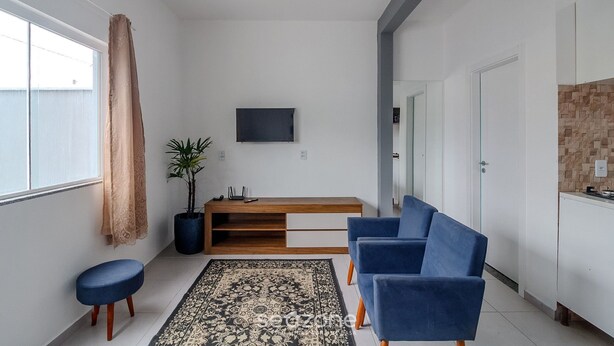 Ein modernes Wohnzimmer mit einer Couch, einem Couchtisch, einem an der Wand befestigten Fernseher und einer Zimmerpflanze.