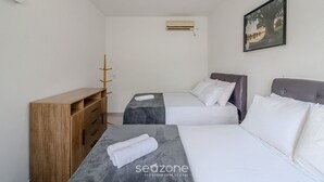 Ein Hotelzimmer mit zwei Betten, einer Holzkommode, einem kleinen Tisch mit einem Handtuch, einer Klimaanlage und einem gerahmten Bild an der Wand.