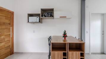 Una habitación moderna con una mesa de madera, un pequeño árbol de Navidad y estantes empotrados con electrodomésticos de cocina.