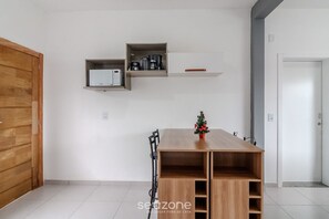 Une pièce moderne avec une table en bois, un petit sapin de Noël et des étagères intégrées où sont rangés les appareils de cuisine.