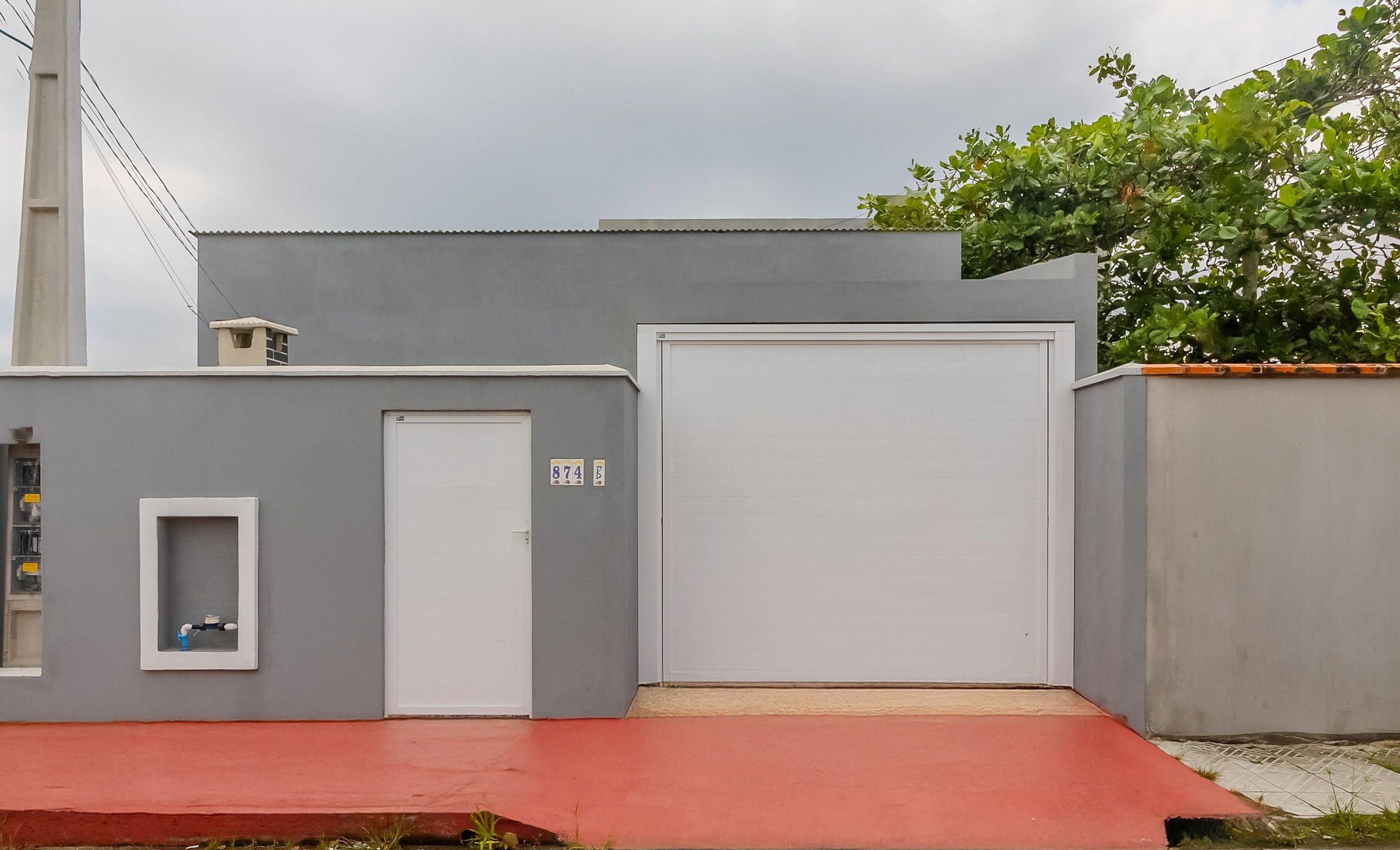 Un edificio gris con una puerta de garaje blanca, un ventanal pequeño y una rampa roja que conduce a la entrada.