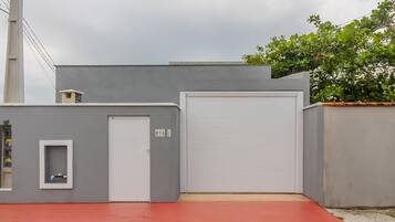 Un edificio gris con una puerta de garaje blanca, un ventanal pequeño y una rampa roja que conduce a la entrada.