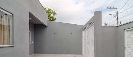 Une cour moderne et minimaliste, dotée d’un sol en béton, entourée de murs gris et agrémentée d’un petit espace recouvert de gravier.