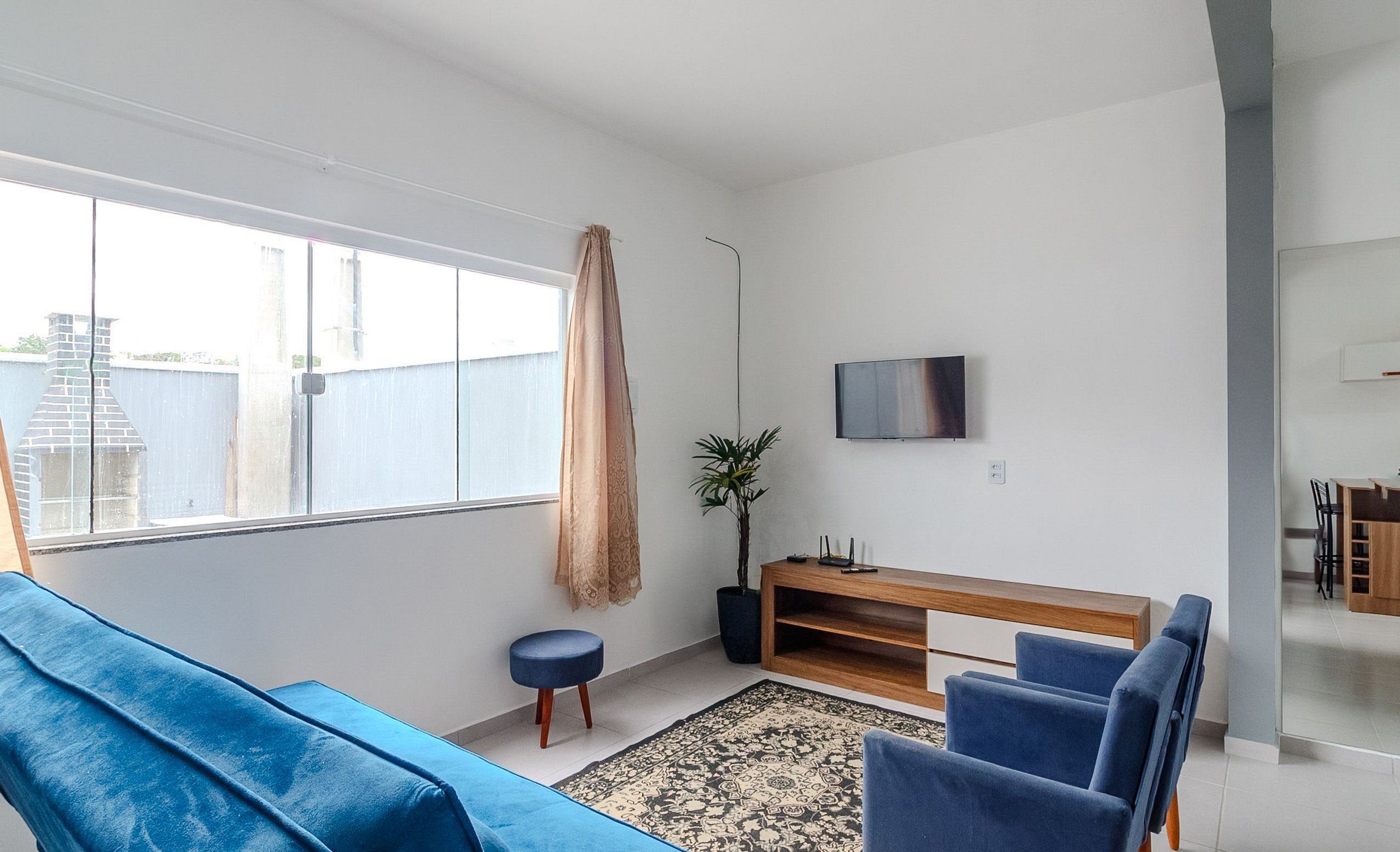 A modern living room with a blue sofa, a wooden TV stand, and a large window.