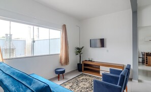 Una sala de estar moderna con un sofá azul, un mueble bajo para televisión de madera y un ventanal grande.