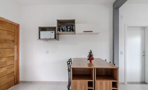 Una habitación moderna con una mesa de madera, un pequeño árbol de Navidad y estantes empotrados con electrodomésticos de cocina.