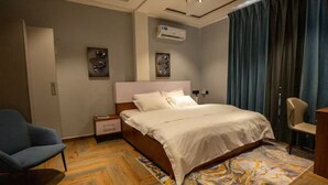 A hotel room with a bed, a chair, an air conditioning unit, and a patterned rug. - EllaVista Residence (Accra)