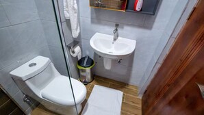 A small bathroom with a toilet, sink, and glass shower enclosure. - EllaVista Residence (Accra)