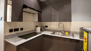 A modern kitchen with dark cabinets, a granite countertop, a stainless steel sink, and a built-in oven. - EllaVista Residence (Accra)