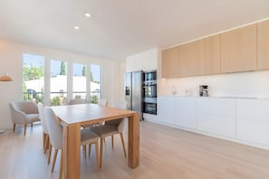 Eine moderne Küche mit weißen Schränken, einem Holztisch und Blick durch große Fenster.