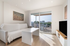 A modern living room with a sofa, a coffee table, a TV, and a balcony with outdoor furniture.