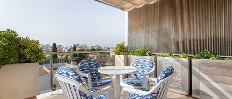 A balcony with white chairs and a small table, overlooking a cityscape.