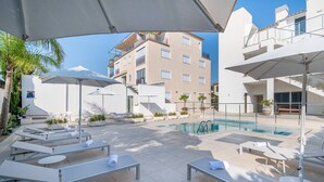 A rooftop pool area with sun loungers and umbrellas, surrounded by buildings. - Apartment 'Las Palmeras 2' with Shared Pool, Wi-Fi and Air Conditioning (Cala Millor)