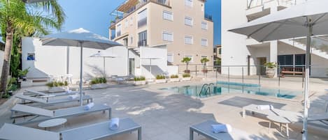 A rooftop pool area with sun loungers and umbrellas, surrounded by buildings.