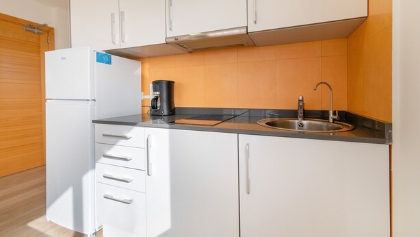 A compact kitchen with white cabinets, a black countertop, a built-in sink, and a coffee maker. - Apartment 'Las Palmeras 2' with Shared Pool, Wi-Fi and Air Conditioning (Cala Millor)