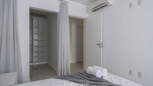 Un dormitorio moderno con cama, una manta gris y una toalla blanca. Hay un vestidor y un equipo de aire acondicionado en la pared.