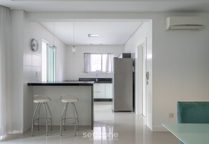 A modern kitchen with a central island, bar stools, and a dining table with a teal chair.