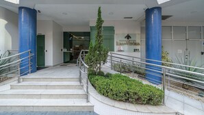 Entrada de un hotel con una escalera que lleva al vestíbulo, columnas azules y un letrero que dice 'Residencial da Vitória'.