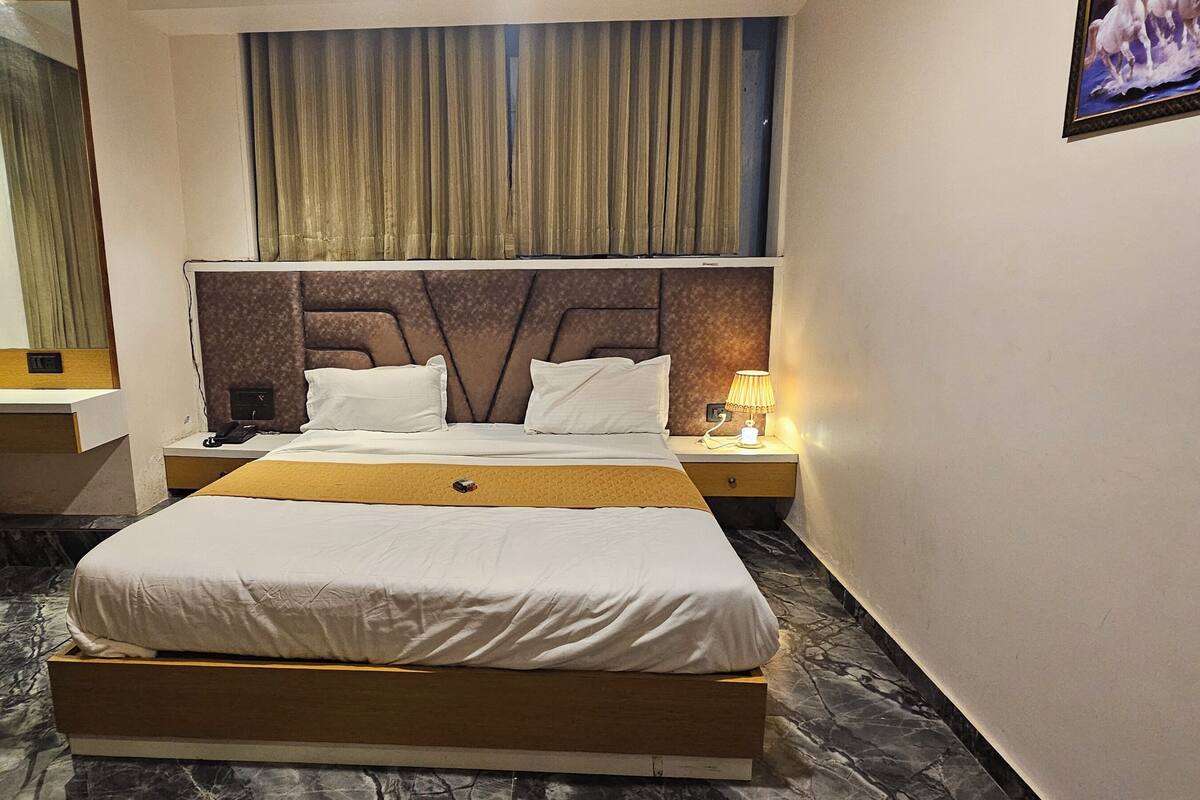 A hotel room with a large bed, a nightstand with a lamp, and a mirror.
